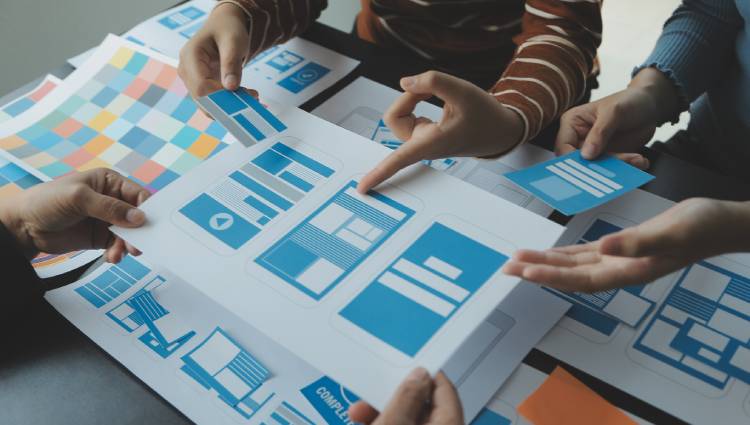 View of a table where a designer is developing a UI/UX application on work sheets